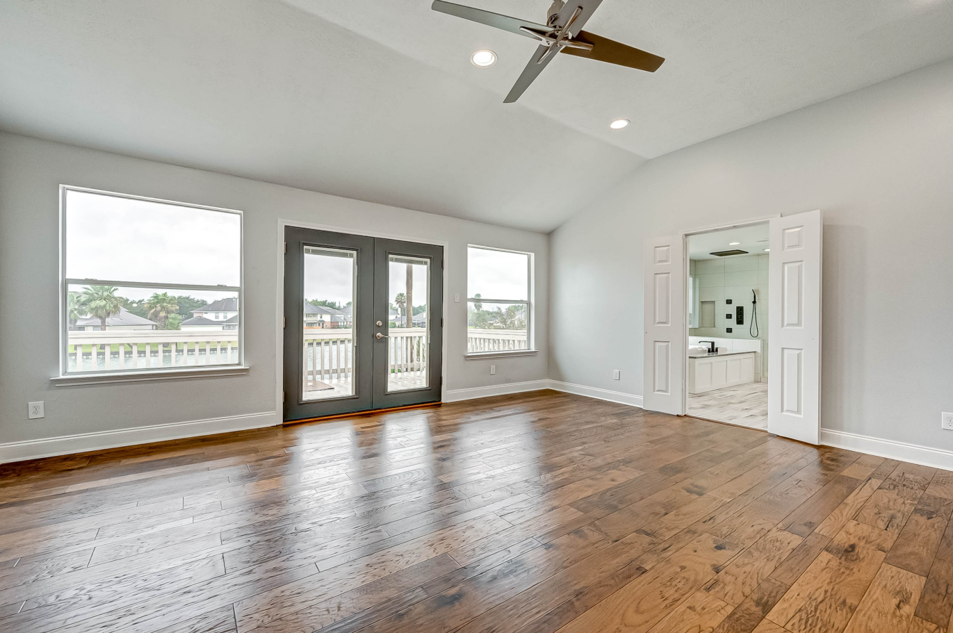 primary bedroom with vaulted ceiling, balcony doors, and hardwood flooring