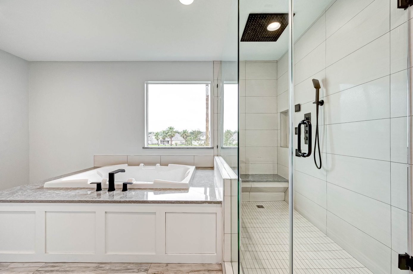 soaking tub with stone countertop surround next to frameless glass walk-in shower with rain head